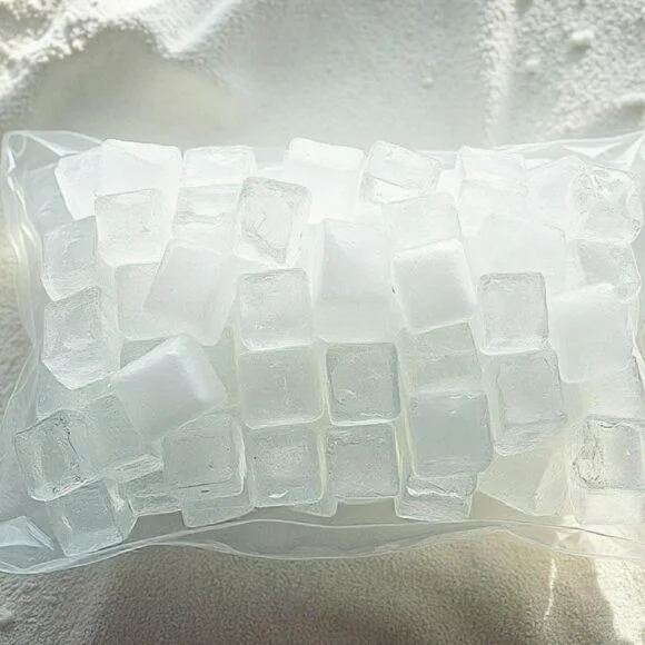 A clear plastic bag filled with transparent ice cubes resting on a textured white surface.