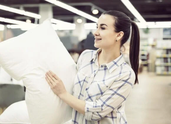 A woman in a plaid shirt holds a white pillow while shopping in a store.