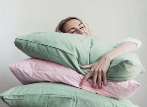 A woman embraces a stack of green and pink pillows while resting her head on the top pillow.