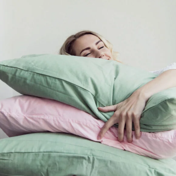 A woman embraces a stack of green and pink pillows while resting her head on the top pillow.