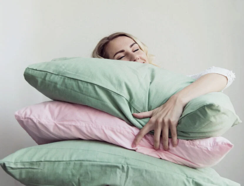 A Complete Guide to Understanding Different Pillow Sizes and Shapes A woman embraces a stack of green and pink pillows while resting her head on the top pillow.