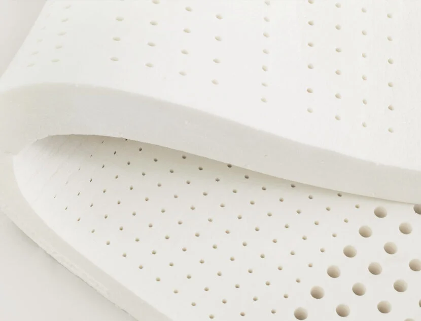 Latex vs. Memory Foam: Which Pillow Material Offers Better Neck Support Close-up of a white, perforated foam mattress topper with small round holes uniformly distributed across its surface. The material appears flexible and slightly folded at the corner.