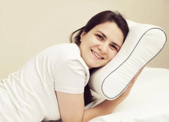 Neck Pain from Sleeping? Memory Foam Pillows Provide Superior Neck Support A person in a white shirt is lying on a bed, smiling, with their head resting on a white pillow to prevent neck pain from sleeping