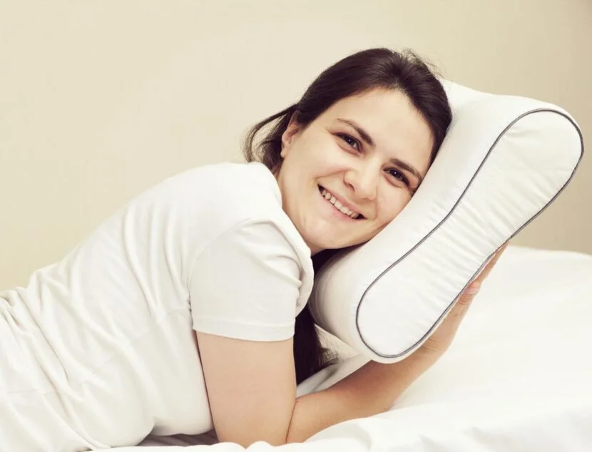 Neck Pain from Sleeping? Memory Foam Pillows Provide Superior Neck Support A person in a white shirt is lying on a bed, smiling, with their head resting on a white pillow to prevent neck pain from sleeping