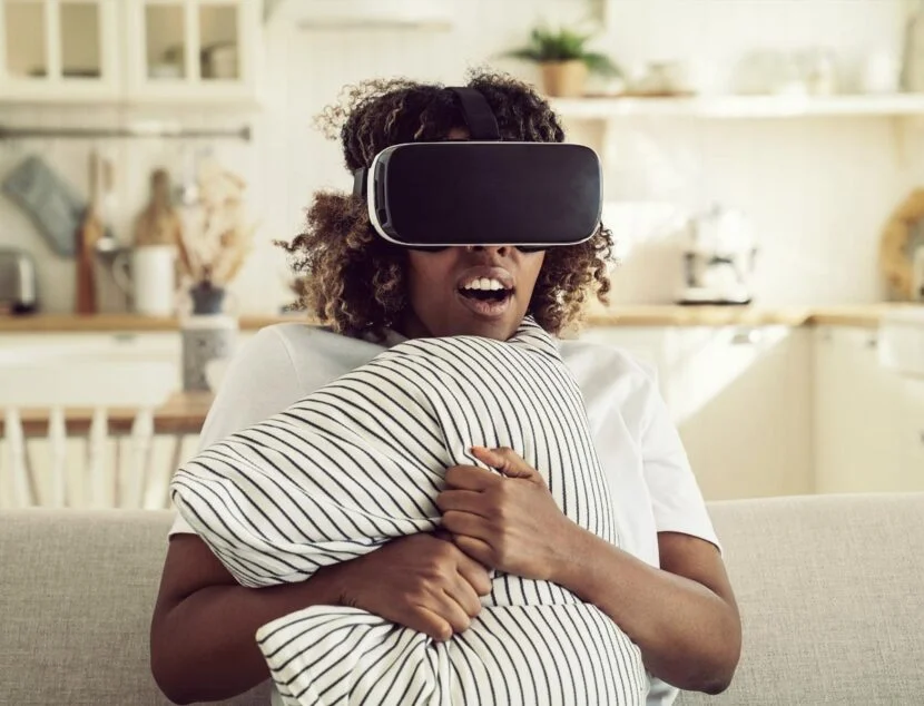 The Science Behind Memory Foam: Why It’s Ideal for Neck Pain Relief A person sitting on a couch wearing a virtual reality headset, holding a striped pillow while experiencing VR content in a cozy, well-lit living room.