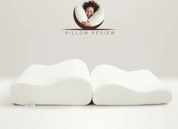 Two memory foam pillows with ergonomic contours are displayed side by side against a light beige background. The words "Pillow Review" and a logo featuring a person hugging a pillow are above them.